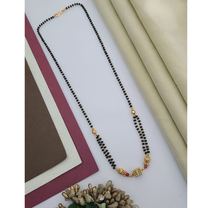Gold-plated mangalsutra with dual black bead chains and intricate golden pendant design, displayed on a flat lay with fabric and decorative props – traditional jewellery by RC Imitation Jewellery.