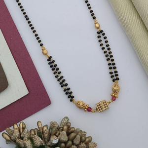 Gold-plated mangalsutra with dual black bead chains and intricate golden pendant design, displayed on a flat lay with fabric and decorative props – traditional jewellery by RC Imitation Jewellery.