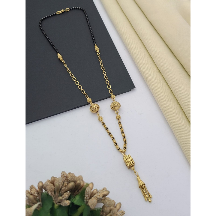 Gold-plated mangalsutra with dual black bead chains and intricate golden pendant design, displayed on a flat lay with fabric and decorative props – traditional jewellery by RC Imitation Jewellery.