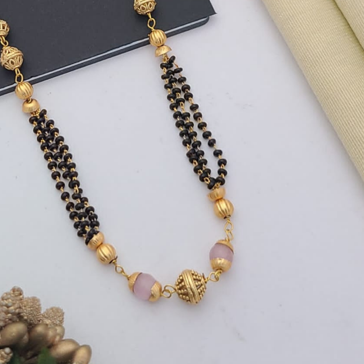 Gold-plated mangalsutra with dual black bead chains and intricate golden pendant design, displayed on a flat lay with fabric and decorative props – traditional jewellery by RC Imitation Jewellery.