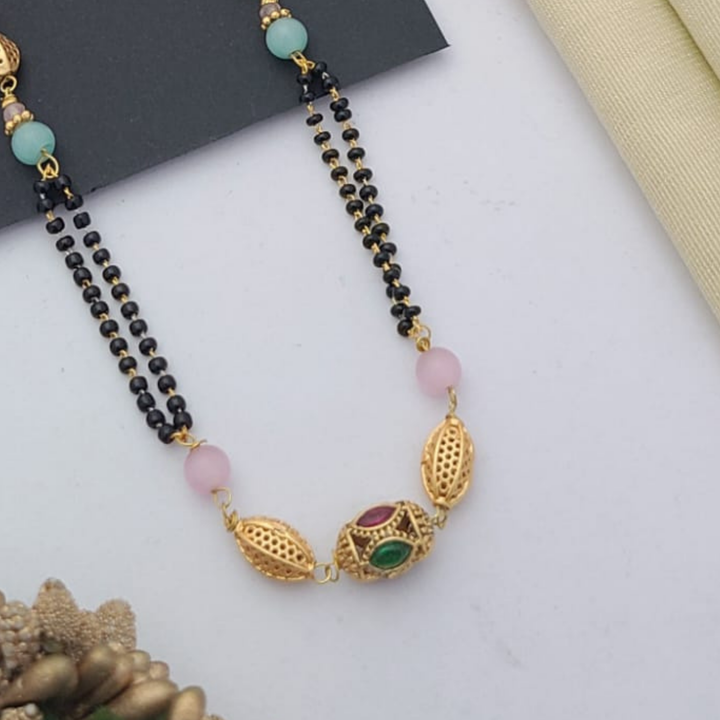Gold-plated mangalsutra with dual black bead chains and intricate golden pendant design, displayed on a flat lay with fabric and decorative props – traditional jewellery by RC Imitation Jewellery.