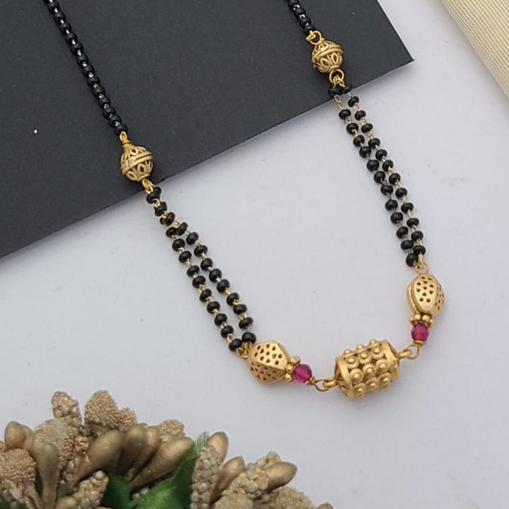 Gold-plated mangalsutra with dual black bead chains and intricate golden pendant design, displayed on a flat lay with fabric and decorative props – traditional jewellery by RC Imitation Jewellery.