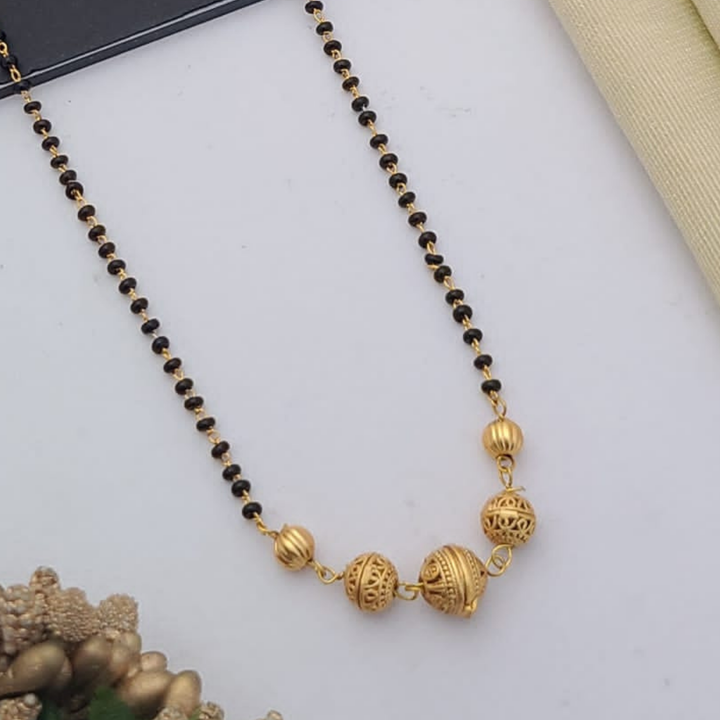 Gold-plated mangalsutra with dual black bead chains and intricate golden pendant design, displayed on a flat lay with fabric and decorative props – traditional jewellery by RC Imitation Jewellery.