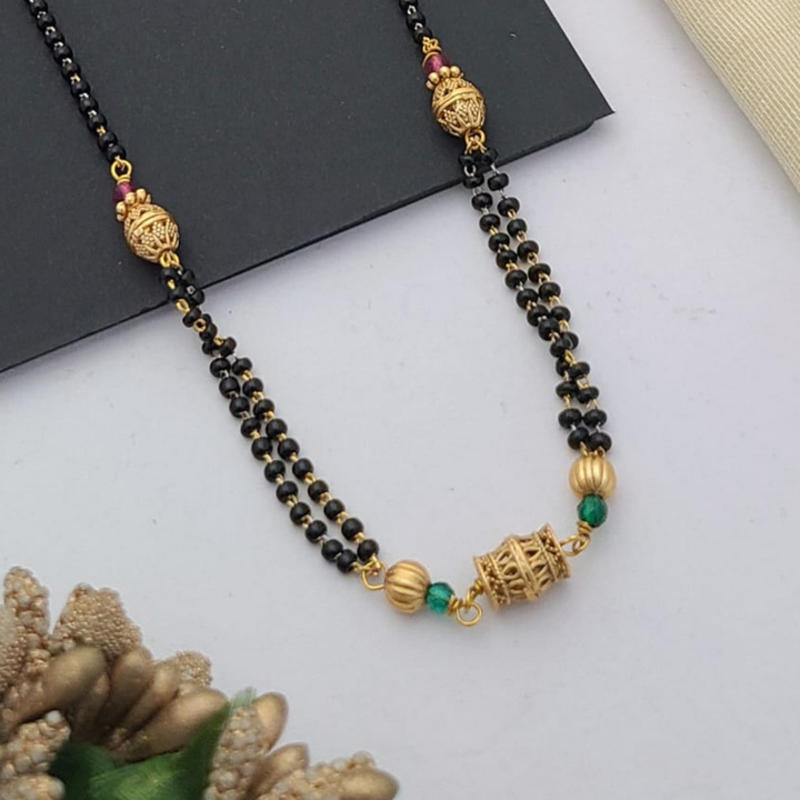 Gold-plated mangalsutra with dual black bead chains and intricate golden pendant design, displayed on a flat lay with fabric and decorative props – traditional jewellery by RC Imitation Jewellery.
