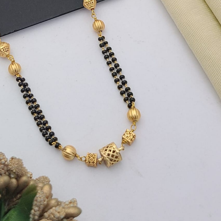 Gold-plated mangalsutra with dual black bead chains and intricate golden pendant design, displayed on a flat lay with fabric and decorative props – traditional jewellery by RC Imitation Jewellery.