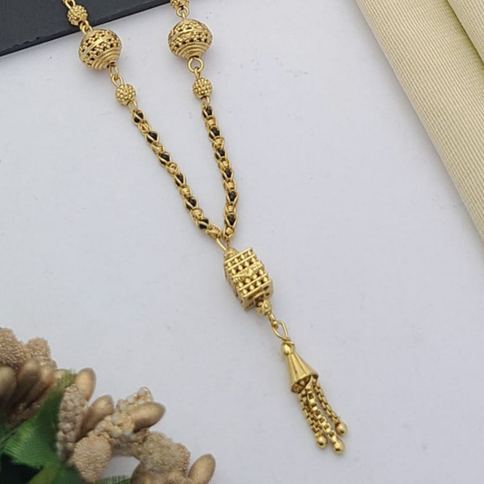 Gold-plated mangalsutra with dual black bead chains and intricate golden pendant design, displayed on a flat lay with fabric and decorative props – traditional jewellery by RC Imitation Jewellery.