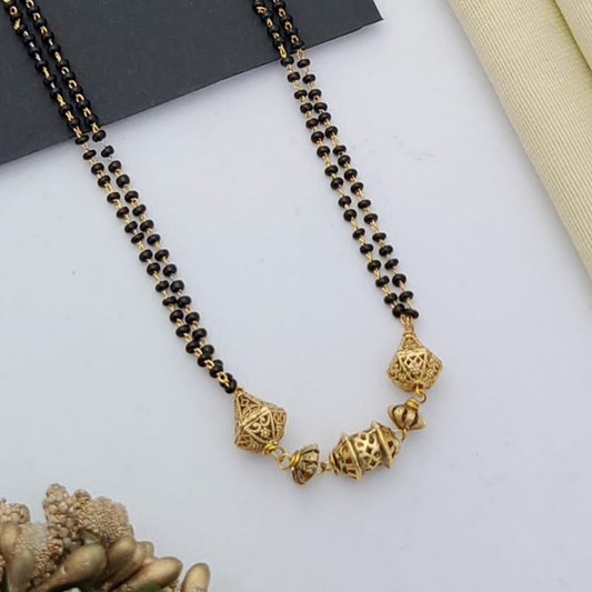 Gold-plated mangalsutra with dual black bead chains and intricate golden pendant design, displayed on a flat lay with fabric and decorative props – traditional jewellery by RC Imitation Jewellery.