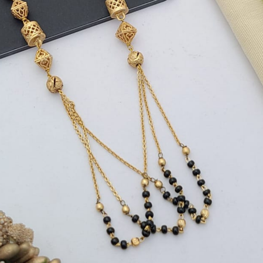 Gold-plated mangalsutra with dual black bead chains and intricate golden pendant design, displayed on a flat lay with fabric and decorative props – traditional jewellery by RC Imitation Jewellery.