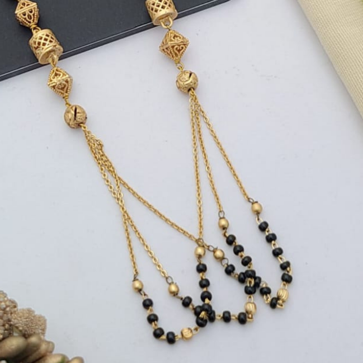 Gold-plated mangalsutra with dual black bead chains and intricate golden pendant design, displayed on a flat lay with fabric and decorative props – traditional jewellery by RC Imitation Jewellery.