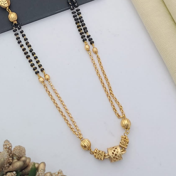 Gold-plated mangalsutra with dual black bead chains and intricate golden pendant design, displayed on a flat lay with fabric and decorative props – traditional jewellery by RC Imitation Jewellery.