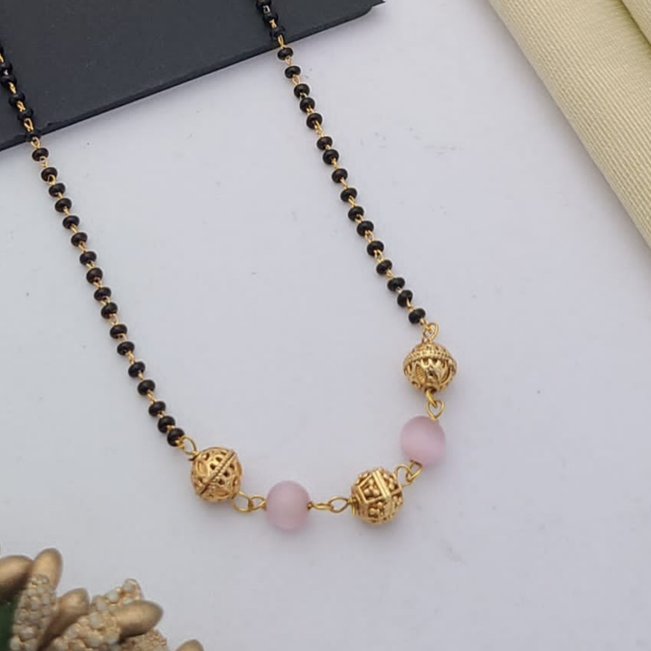 Gold-plated mangalsutra with dual black bead chains and intricate golden pendant design, displayed on a flat lay with fabric and decorative props – traditional jewellery by RC Imitation Jewellery.