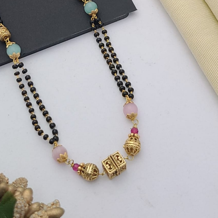 Gold-plated mangalsutra with dual black bead chains and intricate golden pendant design, displayed on a flat lay with fabric and decorative props – traditional jewellery by RC Imitation Jewellery.