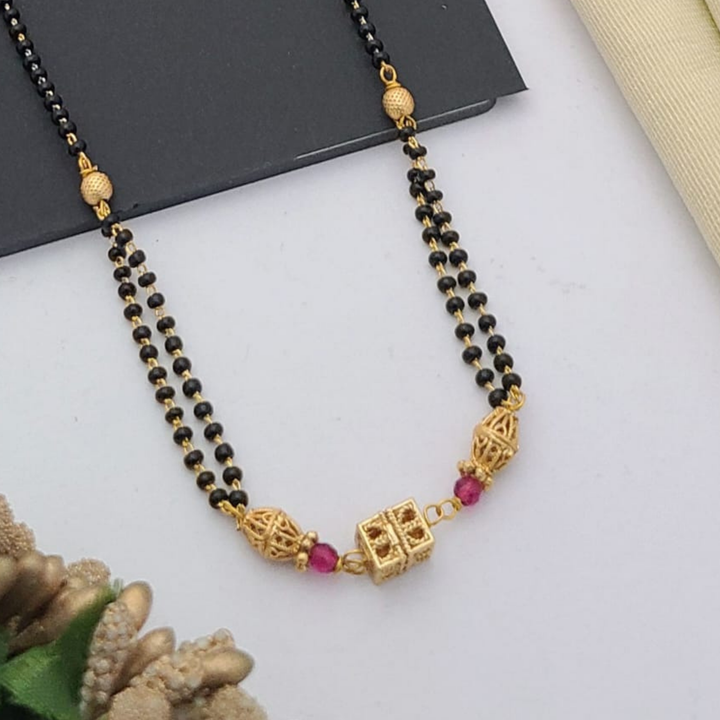 Gold-plated mangalsutra with dual black bead chains and intricate golden pendant design, displayed on a flat lay with fabric and decorative props – traditional jewellery by RC Imitation Jewellery.