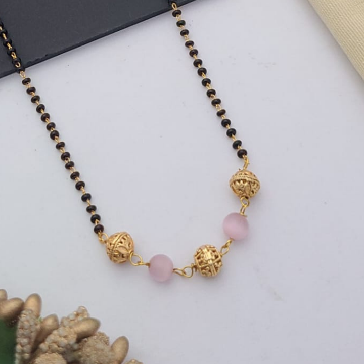 Gold-plated mangalsutra with dual black bead chains and intricate golden pendant design, displayed on a flat lay with fabric and decorative props – traditional jewellery by RC Imitation Jewellery.