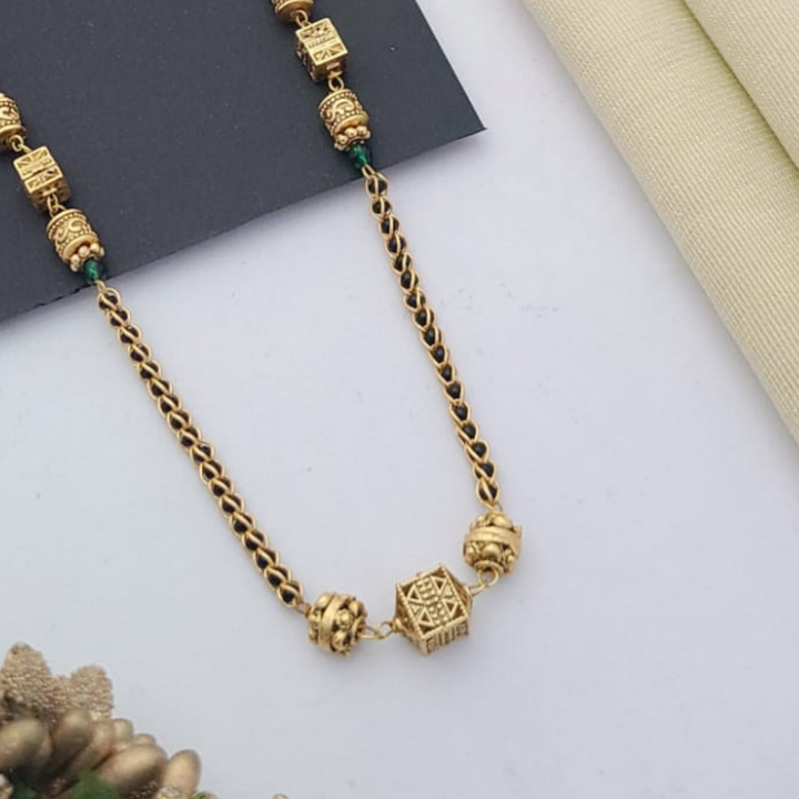 Gold-plated mangalsutra with dual black bead chains and intricate golden pendant design, displayed on a flat lay with fabric and decorative props – traditional jewellery by RC Imitation Jewellery.
