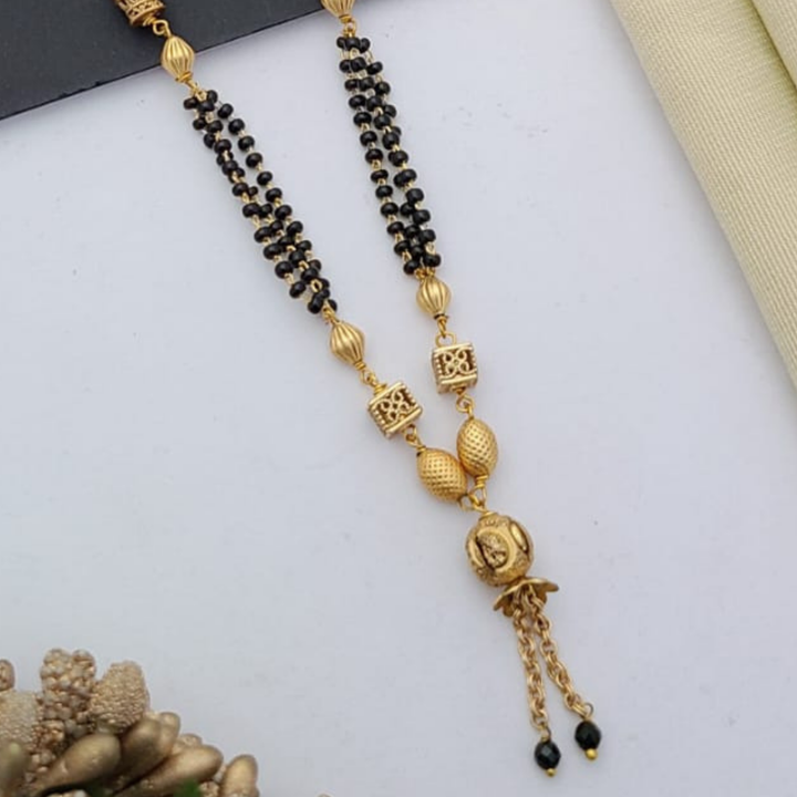 Gold-plated mangalsutra with dual black bead chains and intricate golden pendant design, displayed on a flat lay with fabric and decorative props – traditional jewellery by RC Imitation Jewellery.