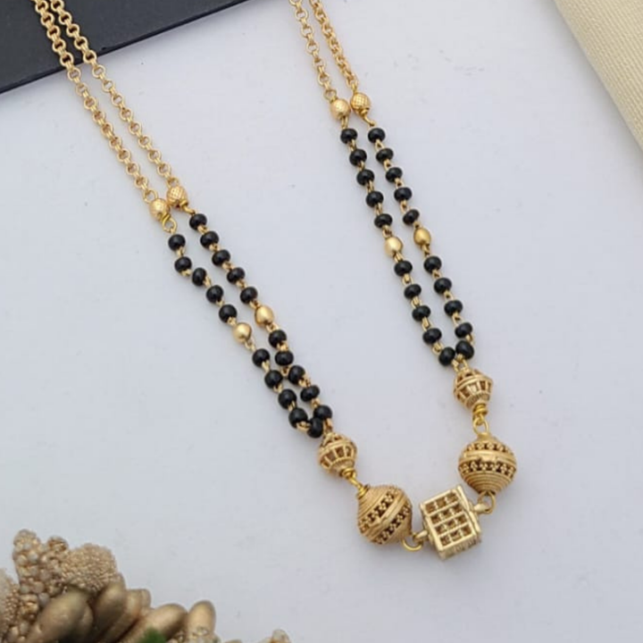 Gold-plated mangalsutra with dual black bead chains and intricate golden pendant design, displayed on a flat lay with fabric and decorative props – traditional jewellery by RC Imitation Jewellery.