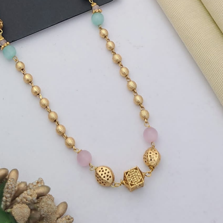 Gold-plated mangalsutra with dual black bead chains and intricate golden pendant design, displayed on a flat lay with fabric and decorative props – traditional jewellery by RC Imitation Jewellery.