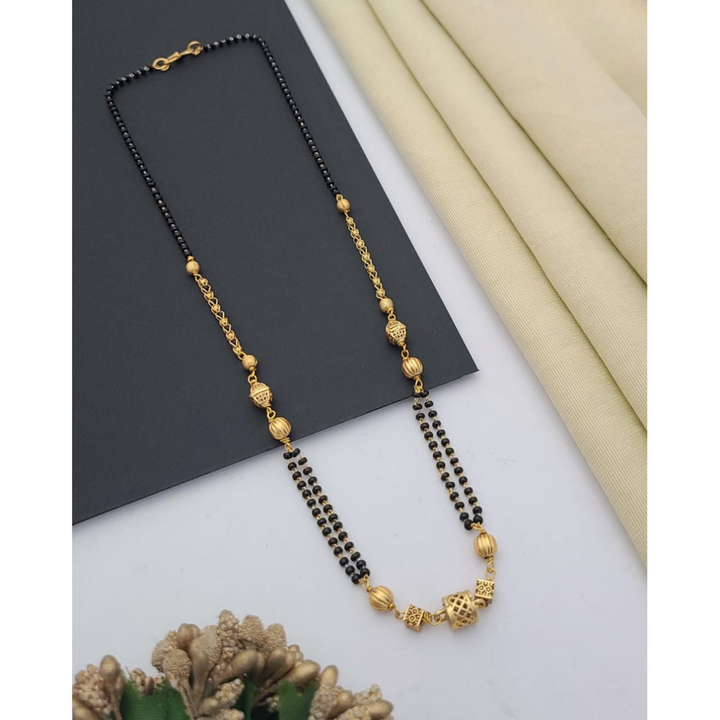 Gold-plated mangalsutra with dual black bead chains and intricate golden pendant design, displayed on a flat lay with fabric and decorative props – traditional jewellery by RC Imitation Jewellery.