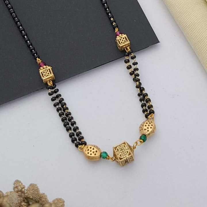 Gold-plated mangalsutra with dual black bead chains and intricate golden pendant design, displayed on a flat lay with fabric and decorative props – traditional jewellery by RC Imitation Jewellery.